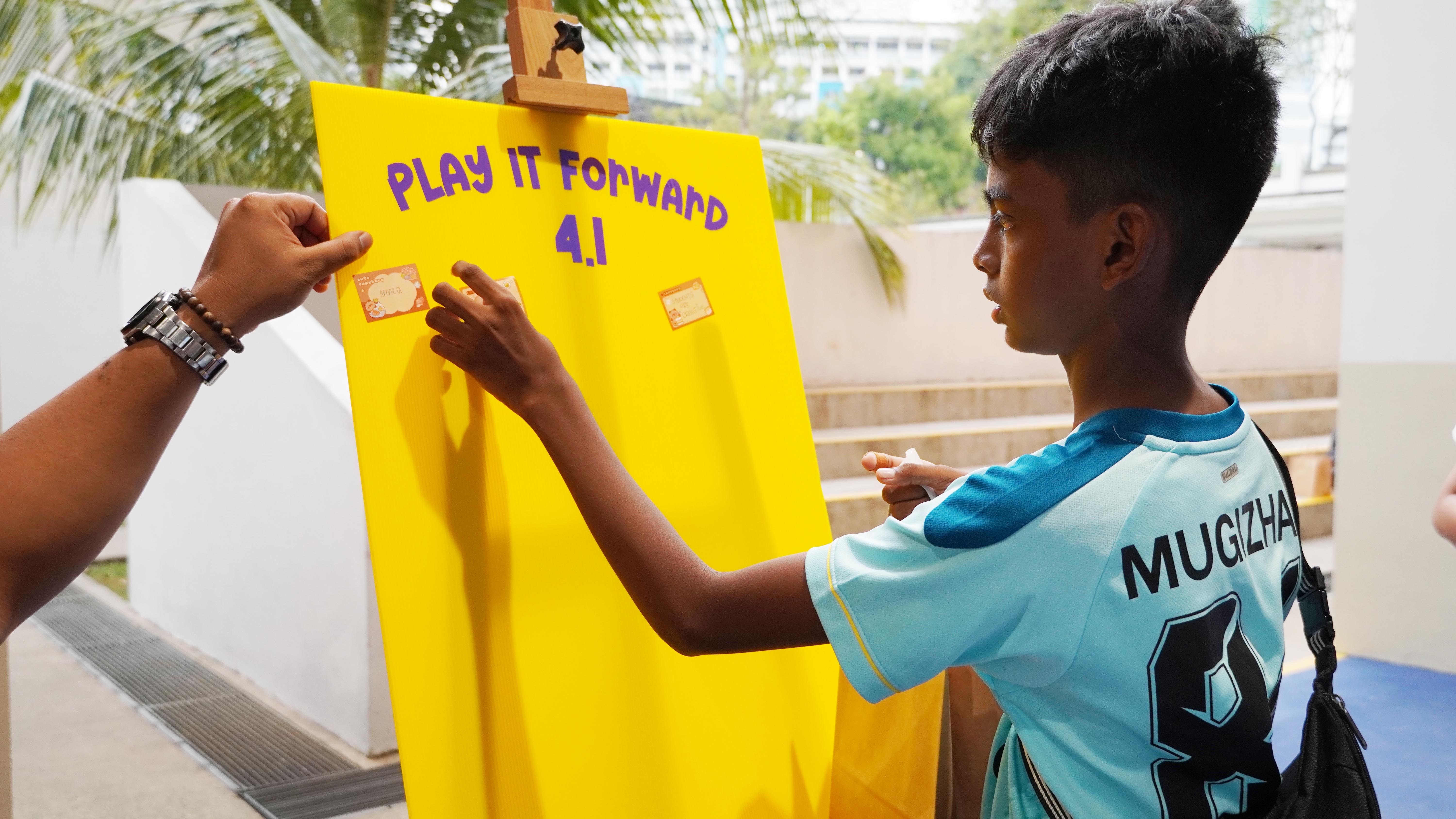 Passing kindness forward! A student adds his contribution to the “Play It Forward” board — because every little act counts.